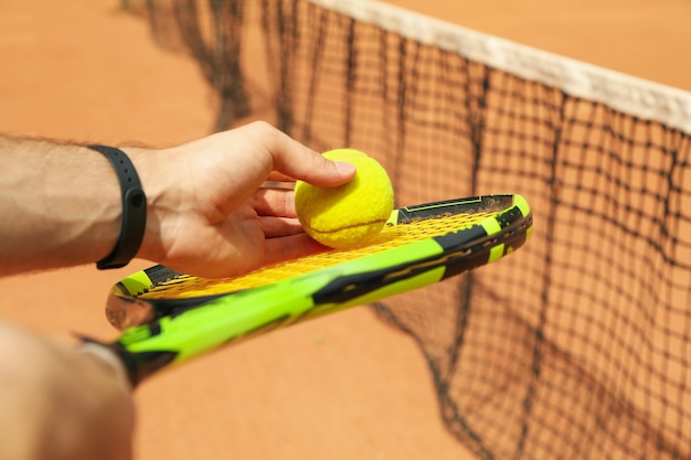 Hombre mantenga la raqueta con pelota de tenis contra la cancha de arcilla