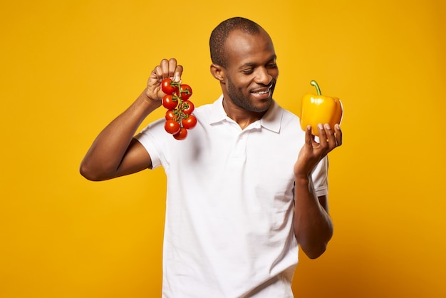 Foto el hombre mantiene un montón de tomates y pimiento amarillo.