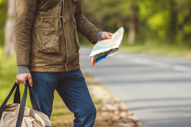 Hombre con mapa y bolso en mano caminando por una carretera