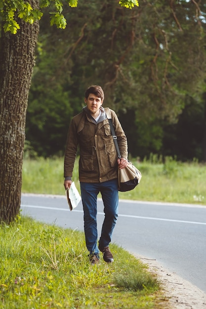 Hombre con mapa y bolso en mano caminando por una carretera