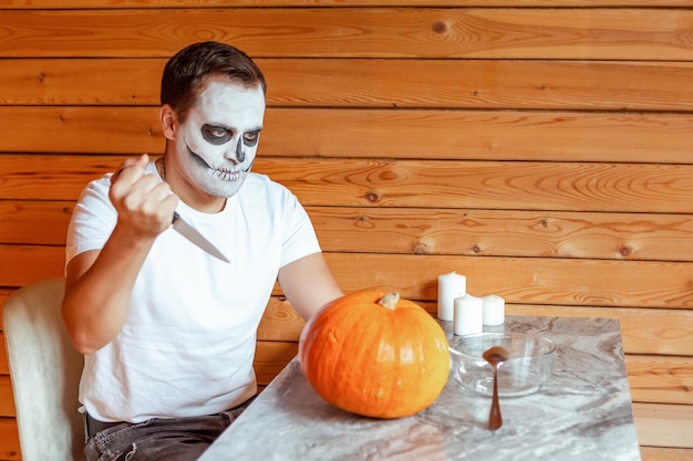 Foto hombre con maquillaje artístico espeluznante de pie preparándose para halloween tallando calabazas