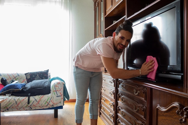 Hombre de maquillaje con barba y pajarita limpiando el polvo de la casa