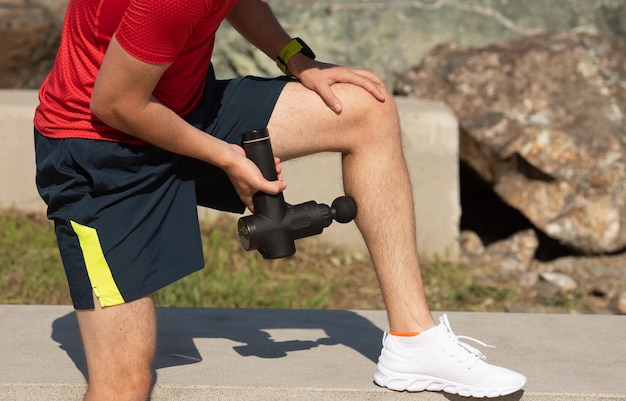 Hombre masajeando el cuerpo con dispositivo de percusión de masaje después del entrenamiento