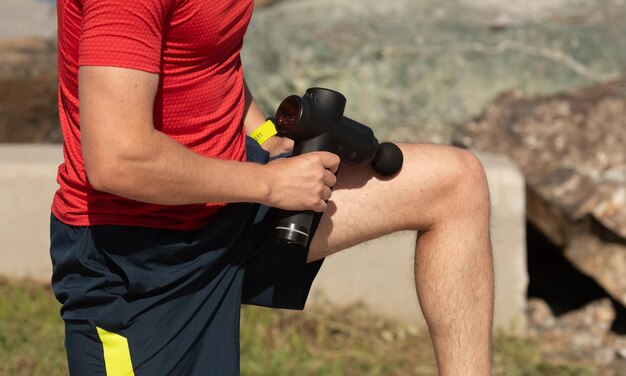 Hombre masajeando el cuerpo con dispositivo de percusión de masaje después del entrenamiento