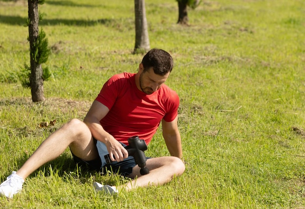 Hombre masajeando el cuerpo con dispositivo de percusión de masaje después del entrenamiento