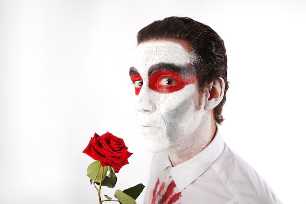 Foto hombre con máscara blanca y camisa sangrienta sostiene una rosa roja frente a un fondo blanco