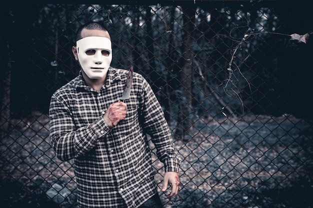 Foto un hombre con una máscara blanca se para frente a una cerca de alambre.