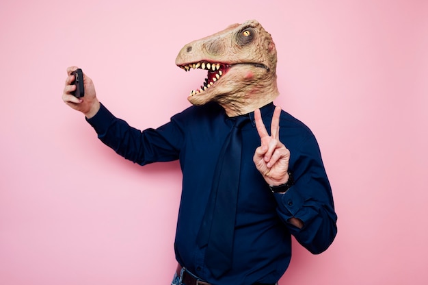 Hombre con máscara de dinosaurio tomando un selfie con smartphone