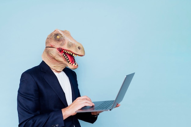 Foto hombre con máscara de dinosaurio usando laptop