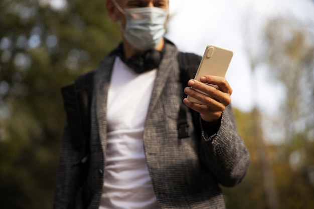 Hombre en máscara estéril con smartphone al aire libre