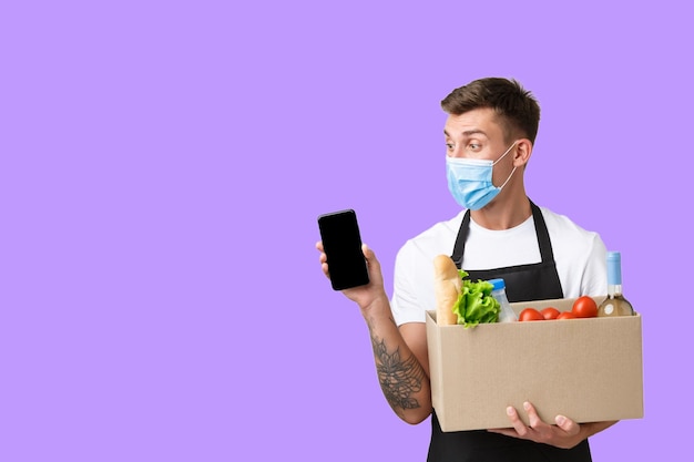 Un hombre con una máscara facial sostiene una caja de comida y una caja de verduras.