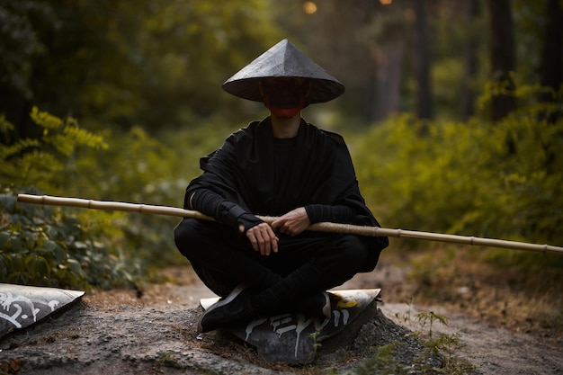 Foto un hombre con una máscara hannya, kimono negro, sombrero negro con un palo de bambú en las manos. samurai surrealista, ninja