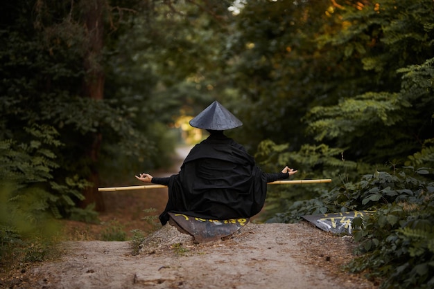 Un hombre con una máscara hannya, kimono negro, sombrero negro con un palo de bambú en las manos. Samurai surrealista, ninja