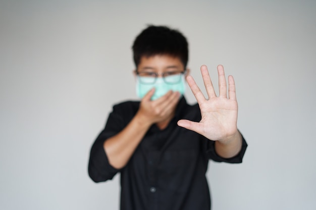 El hombre con máscara de higiene facial para la prevención de la pandemia mundial del virus covid-19. Levante la mano y pare la máscara en la cara, brote de enfermedad coronavirus infeccioso.