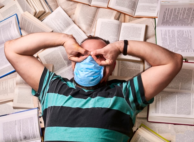 Hombre en máscara médica con muchos libros de papel