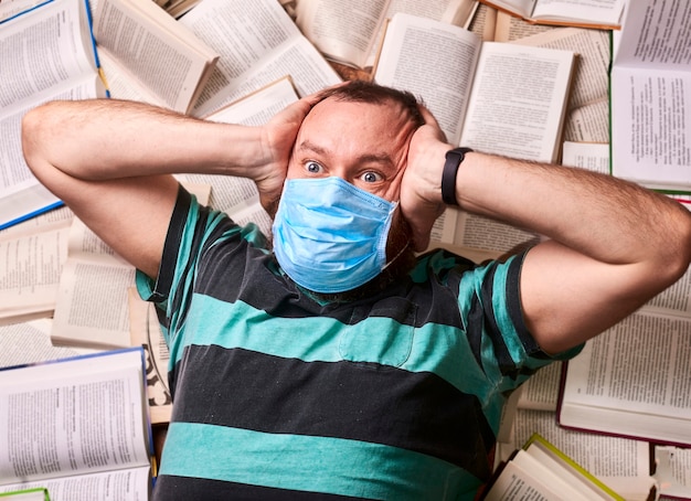Hombre en máscara médica con muchos libros de papel