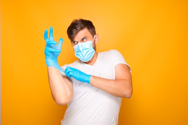 Un hombre con una máscara médica se pone unos guantes azules estériles.