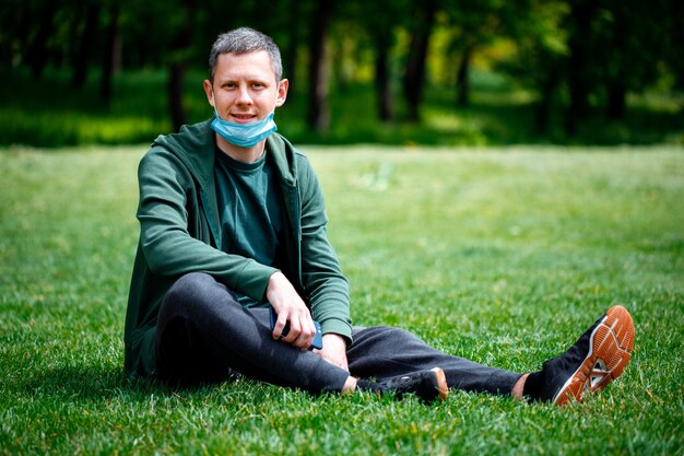 Hombre en una máscara médica sobre la naturaleza. hombre descansando en el parque después de la cuarentena COVID-19