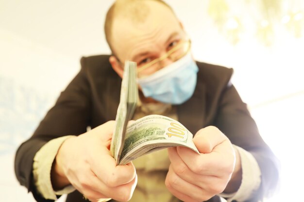 Un hombre con una máscara médica sostiene un paquete de billetes de cien dólares en sus manos El crecimiento económico
