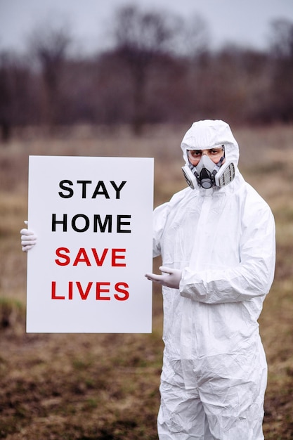 Foto hombre con máscara médica y traje protector con un afiche en las manos concepto epidémico y médico
