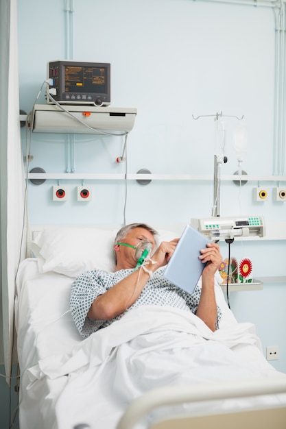 Hombre en la máscara de oxígeno leyendo en la cama