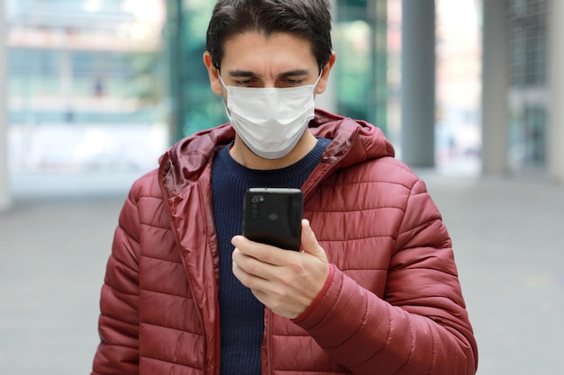 Hombre con máscara protectora leyendo noticias o mensajes en el teléfono inteligente