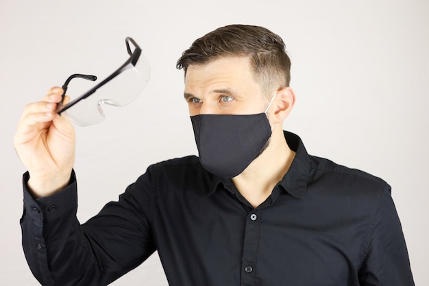 Un hombre con una máscara protectora negra mira en gafas médicas sobre un fondo blanco.