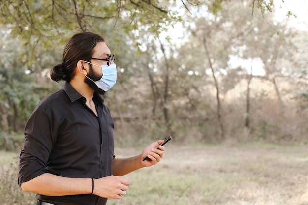 Hombre con una máscara protectora usando un móvil en la naturaleza