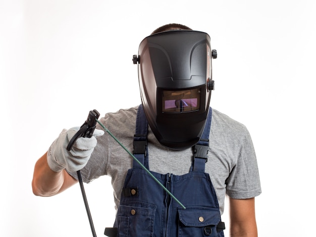 Un hombre con una máscara de soldadura, ropa y guantes robóticos, sosteniendo un cable con un electrodo de soldadura.