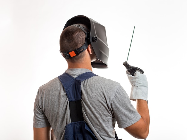 Un hombre con una máscara de soldadura, ropa y guantes robóticos, sosteniendo un cable con un electrodo de soldadura.