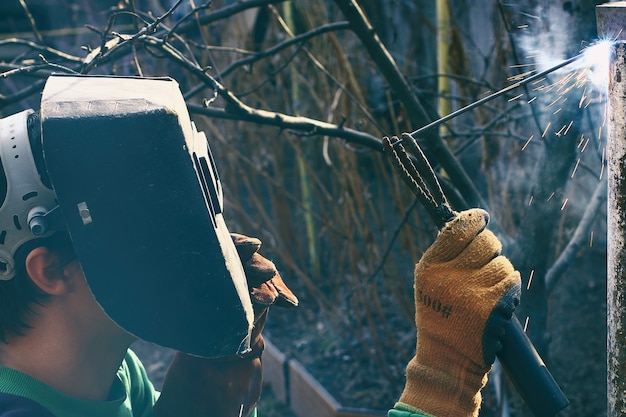 Un hombre con máscara de soldadura con soldadura eléctrica en la mano durante el trabajo de soldadura.