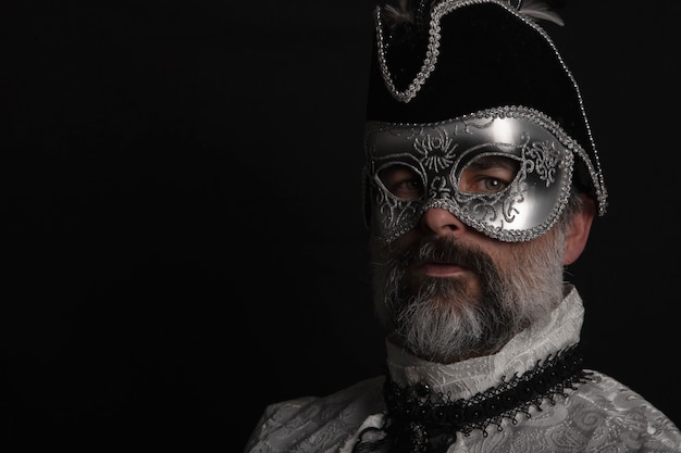 Foto hombre con máscara, sombrero, camisa veneciana y barba sobre fondo negro. concepto de carnaval