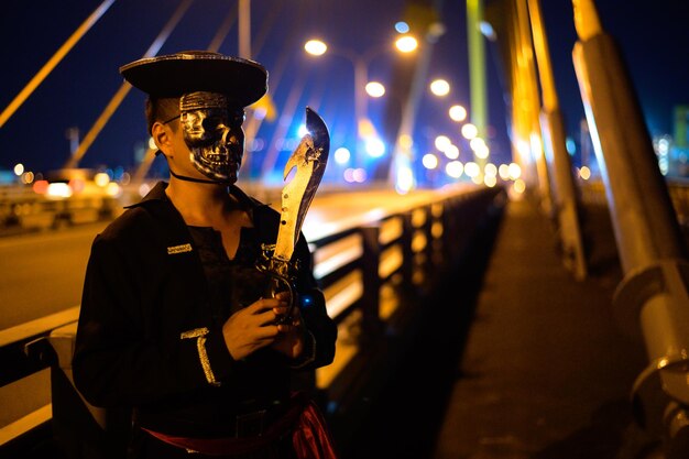Hombre con máscara sosteniendo un cuchillo en el puente por la noche