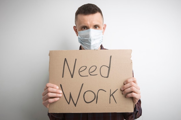 Foto un hombre con una máscara sostiene un cartel con las palabras necesito trabajar. desempleo.