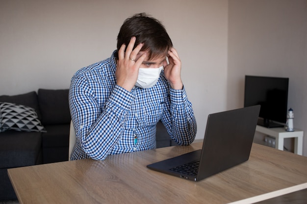 Hombre con máscara trabajando en su computadora portátil desde casa. quedarse en casa, mantenerse a salvo