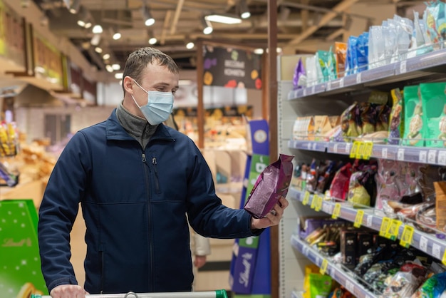 Un hombre con una mascarilla protectora elige productos en la tienda Alimentos y bebidas Comestibles