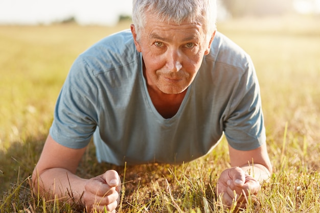 un hombre mayor de unos 50 años hace flexiones de césped verde mientras se recrea en la naturaleza, no se olvida del deporte