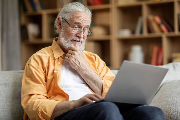 Hombre mayor alegre que usa la computadora portátil en casa