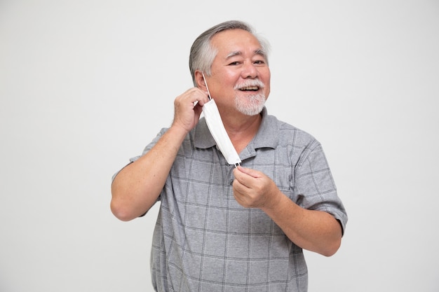 Hombre mayor asiático quitarse la mascarilla protectora aislado sobre fondo blanco.