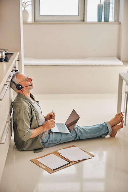 Hombre mayor en auriculares y con computadora portátil trabajando desde casa