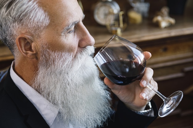Hombre mayor barbudo elegante y guapo bebiendo vino tinto
