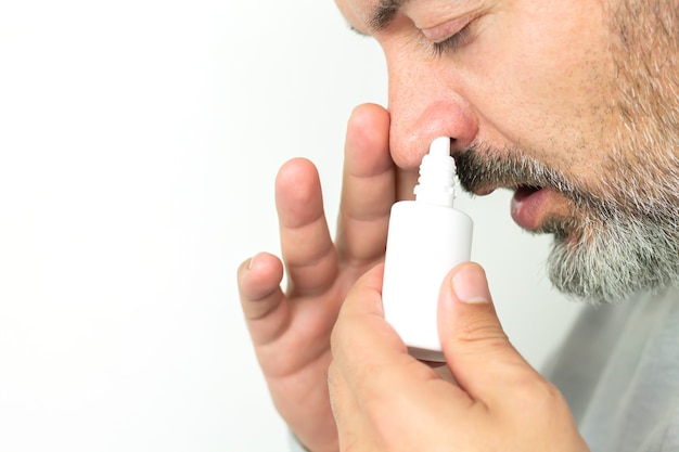 Hombre mayor barbudo que aplica el aerosol para la nariz que moquea. Tratamiento de resfriados y concepto de gripe.