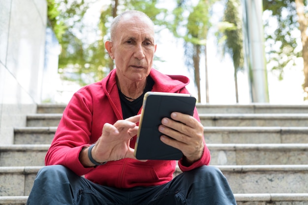 Hombre mayor Calvo con tableta digital mientras está sentado en la escalera