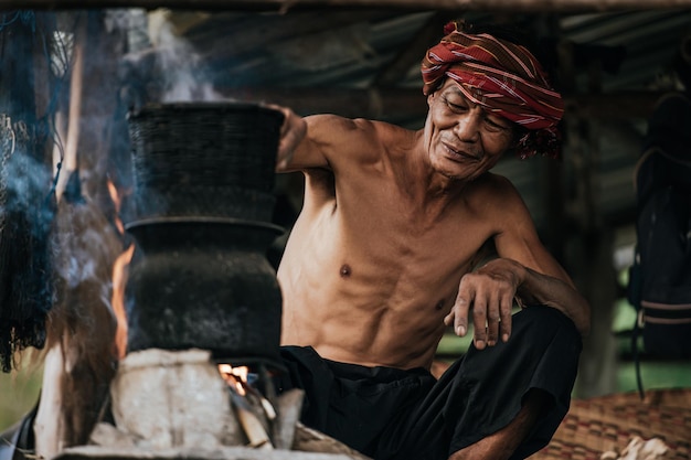 Hombre mayor sin camisa y taparrabos de turbante arroz pegajoso al vapor con una estufa de leña según la vida de la gente rural, espacio de copia, escena rural del campo en Tailandia