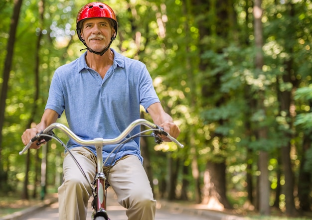 El hombre mayor en casco está montando la bicicleta en parque.