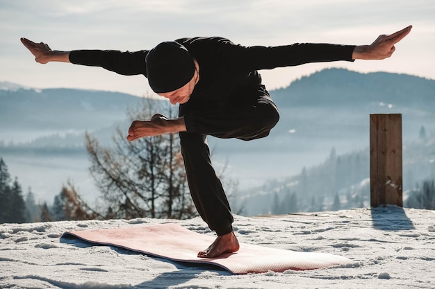 Hombre mayor caucásico haciendo ejercicios de yoga frente a una increíble puesta de sol en las montañas de invierno
