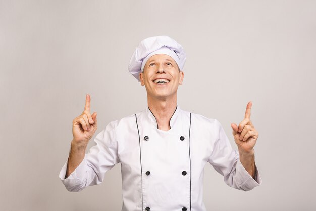 Hombre mayor del cocinero aislado que muestra un espacio de la copia con señalar los dedos para arriba.