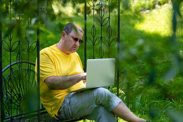 Hombre mayor con computadora portátil que trabaja afuera en el concepto de oficina en casa verde jardín