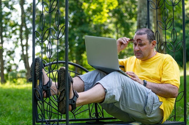 Hombre mayor con computadora portátil que trabaja afuera en el concepto de oficina en casa verde jardín