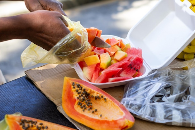 Hombre mayor cortando fruta fresca en un recipiente de plástico para un cliente